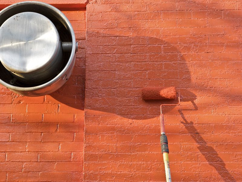 A paint roller loaded with terracotta paint on a freshly painted orange brick wall