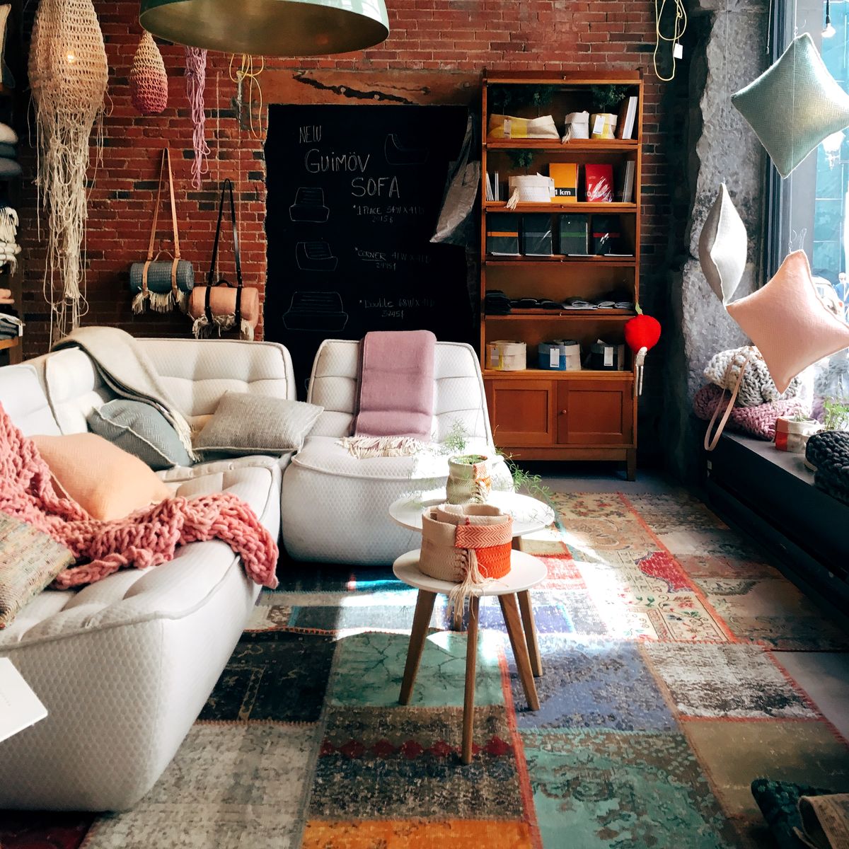 A warm living room with a red brick wall, a white sofa, a rug, plants and green pendant lamps