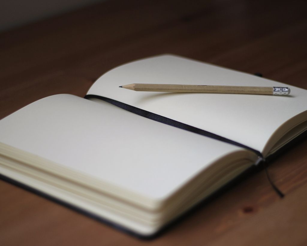 An open blank notebook with a pencil resting across it on a wooden desk