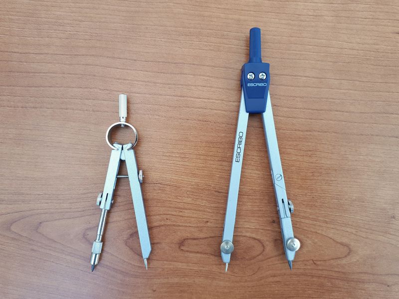 Two school drawing compasses lying side by side on a desk