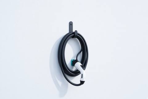 A coiled charging cable hanging on a hook against a white wall.