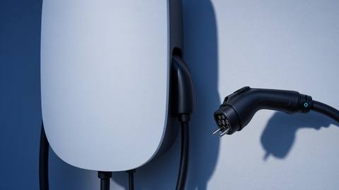 A Type 2 plug nearing the holster of a plain white wall charger.