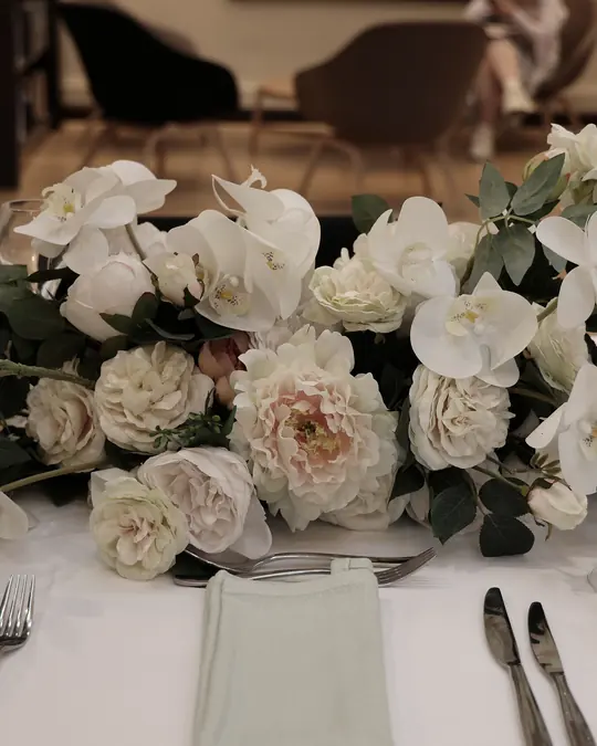 A long centrepiece of white roses and orchids on a table set with silver cutlery and glasses