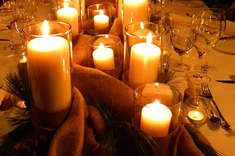 Rows of lit candles in glass holders along a dining table