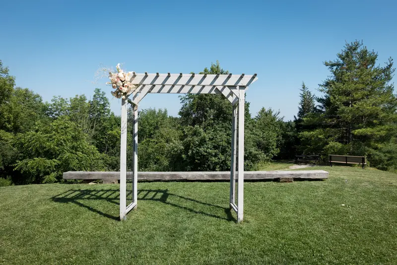 A white wooden pergola standing on a mown lawn with trees behind