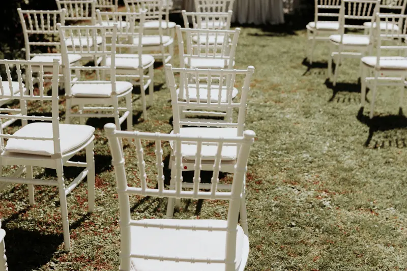 White ceremony chairs with cushions set out on a garden lawn scattered with petals