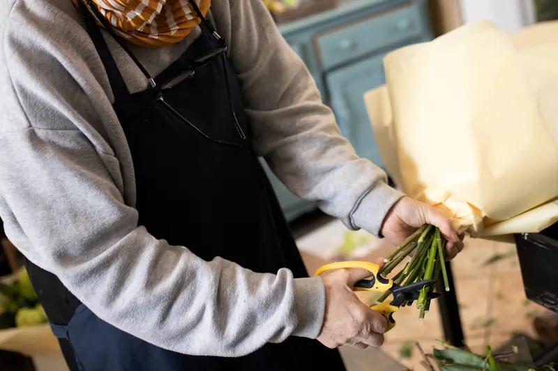 A florist in an apron trimming the stems of a wrapped bouquet