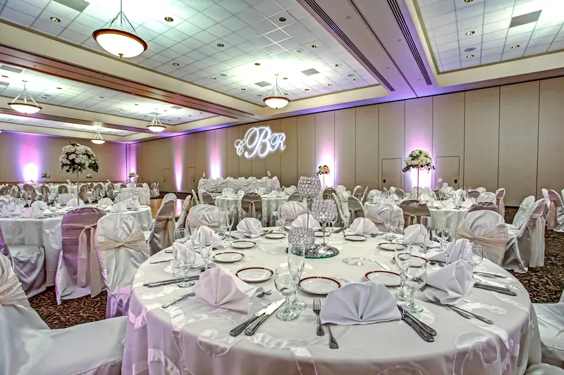 A hotel ballroom set with round tables, white cloths and soft purple uplighting