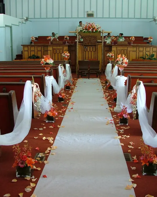 A chapel aisle with a white runner and pews tied with white bows and flowers