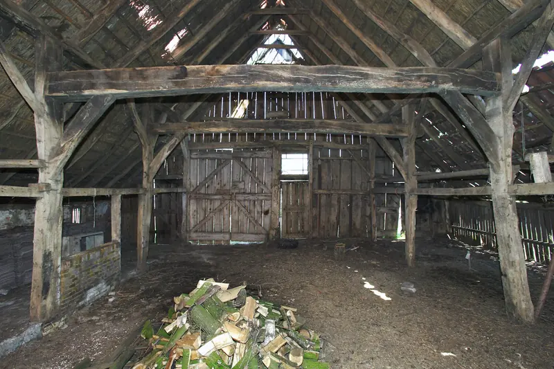 The timber-framed interior of an old barn with its roof trusses exposed