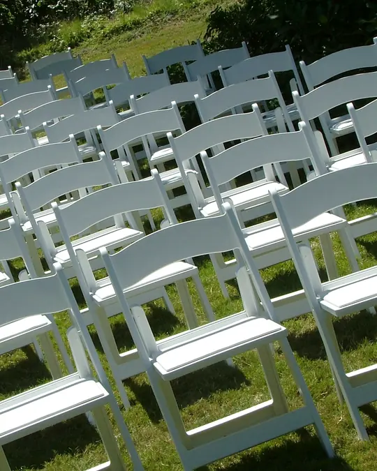 Rows of white folding chairs on a grassy slope, set for an outdoor ceremony