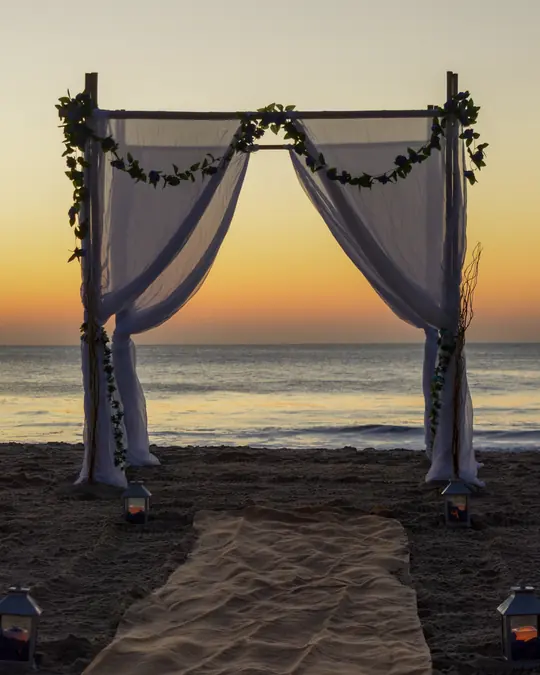 A draped wedding arch on a beach at sunrise