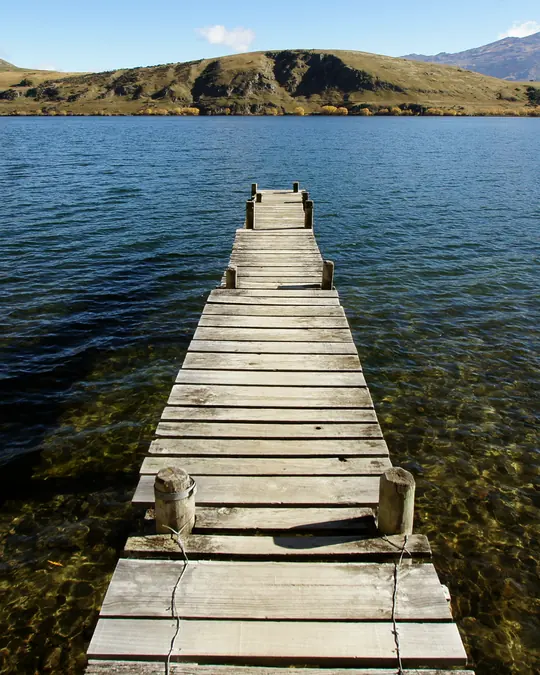 A wooden jetty running out into a calm lake with hills behind