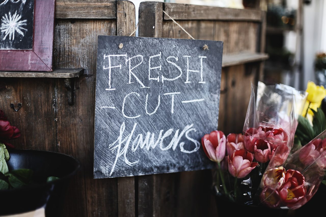 A chalkboard sign reading “Fresh cut flowers” on a wooden stall beside tulips and proteas