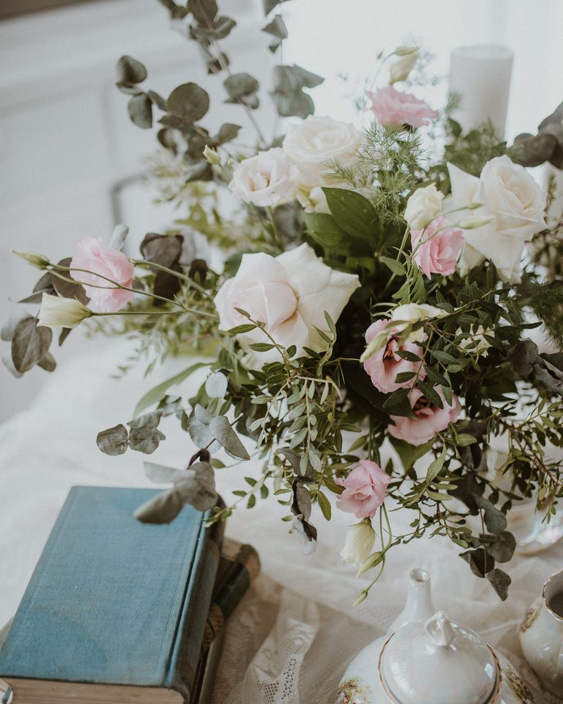 A loose arrangement of soft pink and white roses with greenery on a table beside books