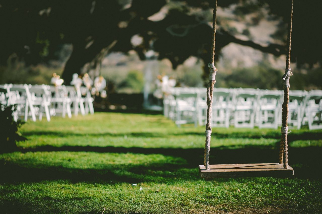Rows of white chairs on a lawn under trees, with a rope swing in the foreground