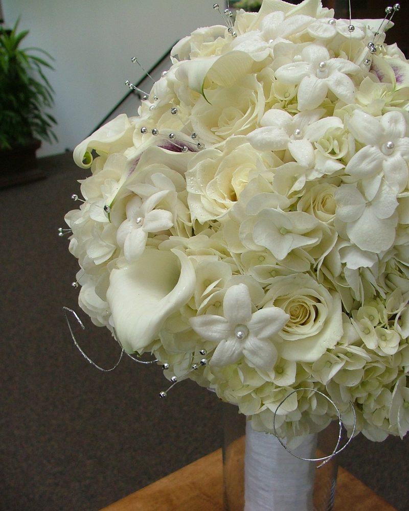 A round bridal bouquet of white roses, lilies and cream flowers