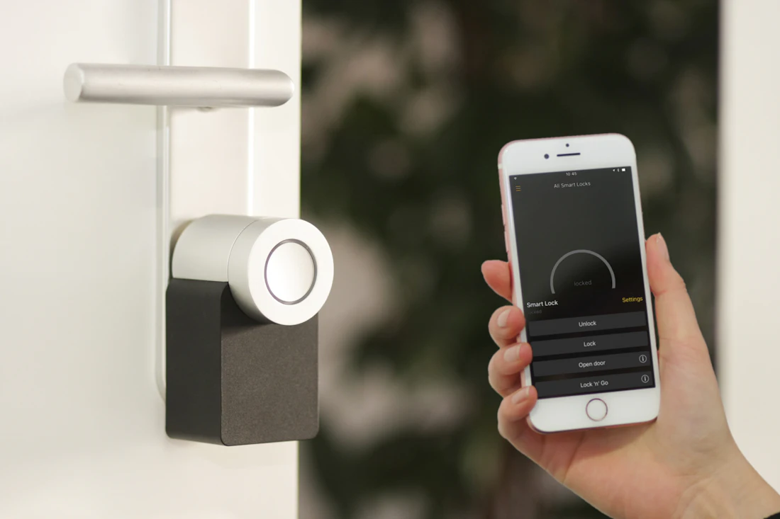 A hand with a phone next to a smart door lock